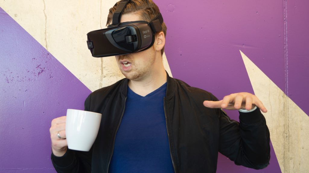 Uomo che indossa sulla testa il visore per la realtà virtuale e ha in mano un tazza di caffè